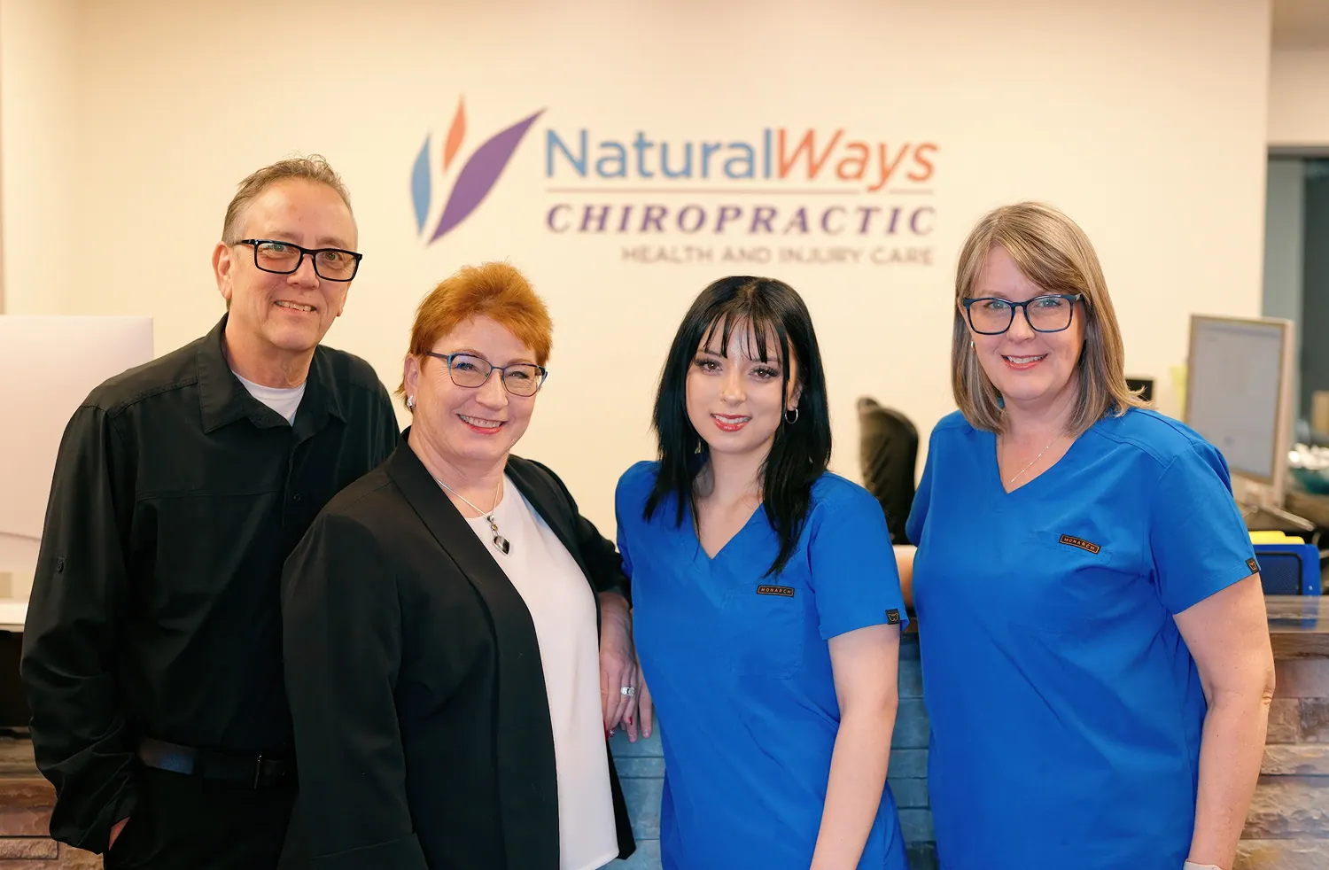 The Natural Ways Chiropractic team in front of the reception sign